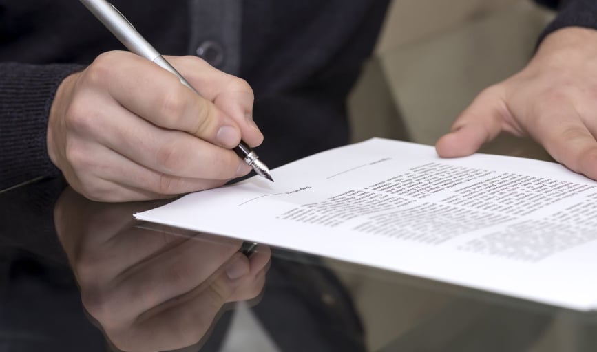 Contract being signed with a fountain pen across a glass table