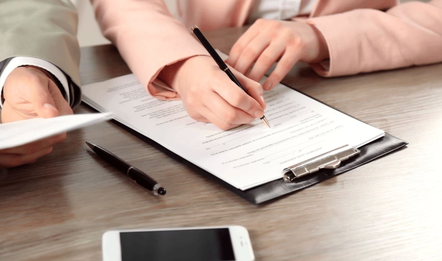 Client signing a document on a clipboard while the notary looks on